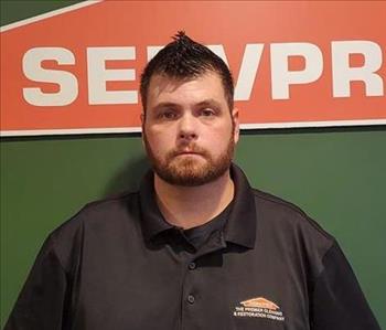 A portrait picture of a male named Jason Dean in front of a green wall with a SERVPRO orange house logo 