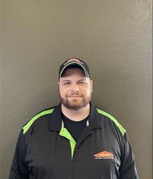 A portrait picture of a male named Jason Dean in front of a green wall with a SERVPRO orange house logo 