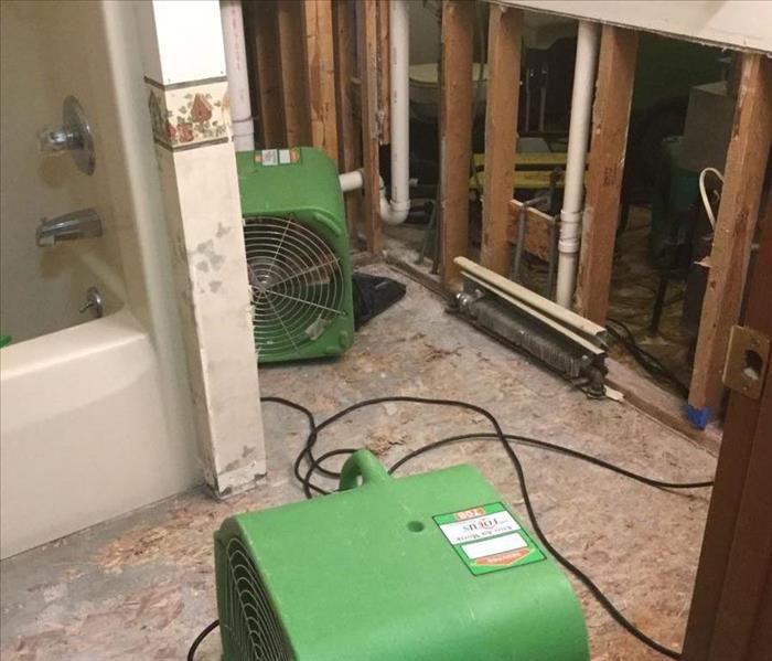 a bathroom with flooring and toilet removed, drywall cut out in bottom of walls and SERVPRO equipment set up to dry. 