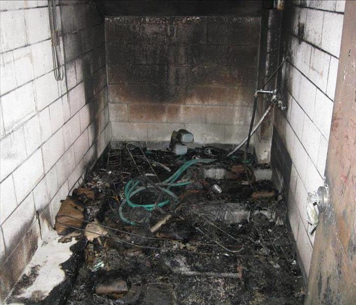 Boiler room after a fire with walls and floor damaged. You can see a lot of hoses and other items burned on floor