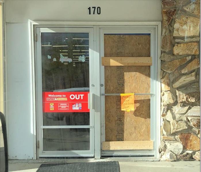 image of front door to a store with right side glass door boarded up. 