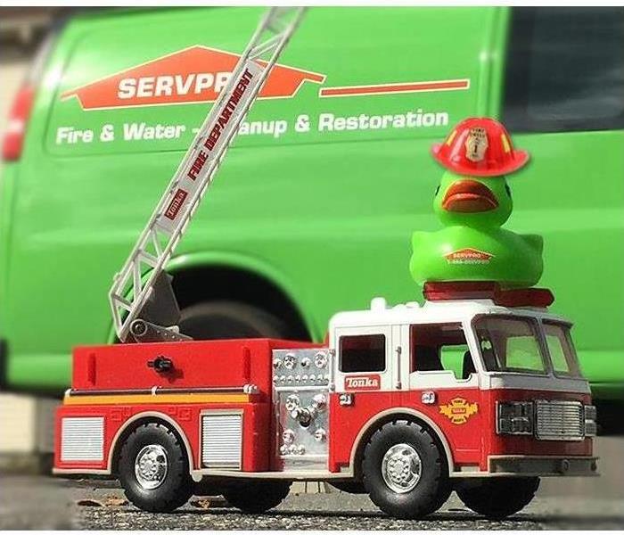 A toy fire truck with the SERVPRO duck on top of it and a SERVPRO van in background