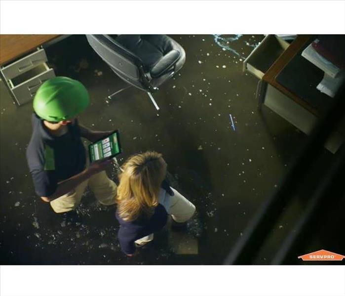 A SERVPRO employee with an iPad walking with a customer thru and office which looks wet with water from sprinkler system